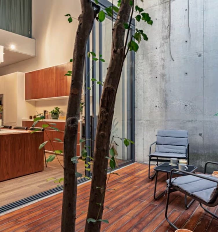 Wooden deck in an inner courtyard with trees, outdoor chairs and the kitchen behind glass